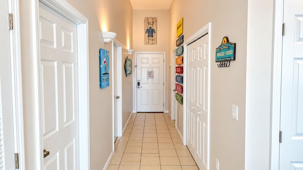 A hallway with white doors, a tiled floor, and wall-mounted signs.