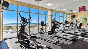 Un gimnasio con máquinas de cardio y un amplio ventanal con vistas a la playa.