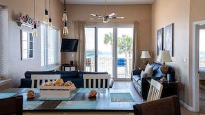 A living room with a sofa, a dining table with a fruit basket, a TV, and a ceiling fan.
