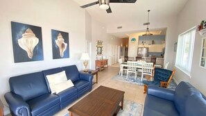 Una sala de estar con un sofá azul, una mesa de centro de madera y una zona de comedor con sillas blancas.