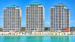 Three high-rise hotels with balconies, a beach in the foreground, and clear skies.