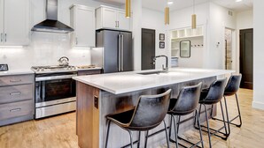 A modern kitchen with stainless steel appliances, a large island with bar stools, and pendant lighting.