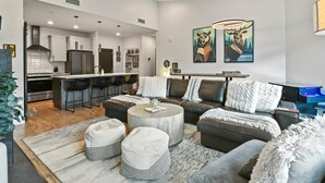 A modern living room with a sectional sofa, ottomans, a coffee table, and a dining area with bar stools.