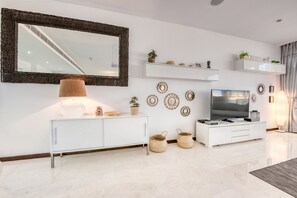 A modern living room with a large mirror, white cabinetry, a flat-screen TV, decorative wall art, and a staircase in the background.