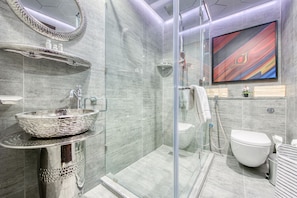 Een moderne badkamer met een douchecabine van glas, een wit wastafelmeubel met een decoratieve kom en een grote spiegel.