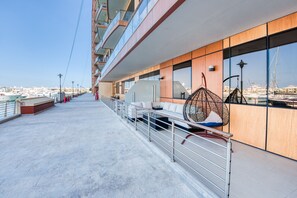 A modern outdoor balcony with a view of the marina, featuring a seating area with a hanging chair and a sofa.