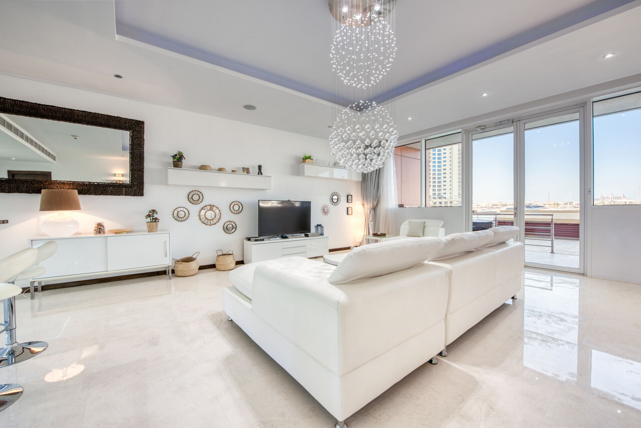A modern living room with a white sofa, a TV, and a large chandelier.