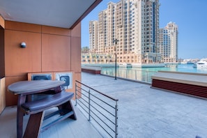 Een balkon met een tafel en stoelen, met uitzicht op een jachthaven met boten en hoogbouw.