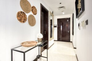 A hallway with a glass console table, woven wall art, and a dark wooden door.