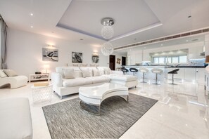 Un salon spacieux avec un canapé blanc, une table basse en verre et un lustre moderne.