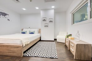 Una camera da letto con un letto di legno, un tappeto decorato, una sedia bianca, un comodino con una lampada e opere d'arte raffiguranti paesaggi urbani.