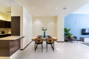 A modern living room with a dining area, a kitchen, and a TV mounted on the wall.