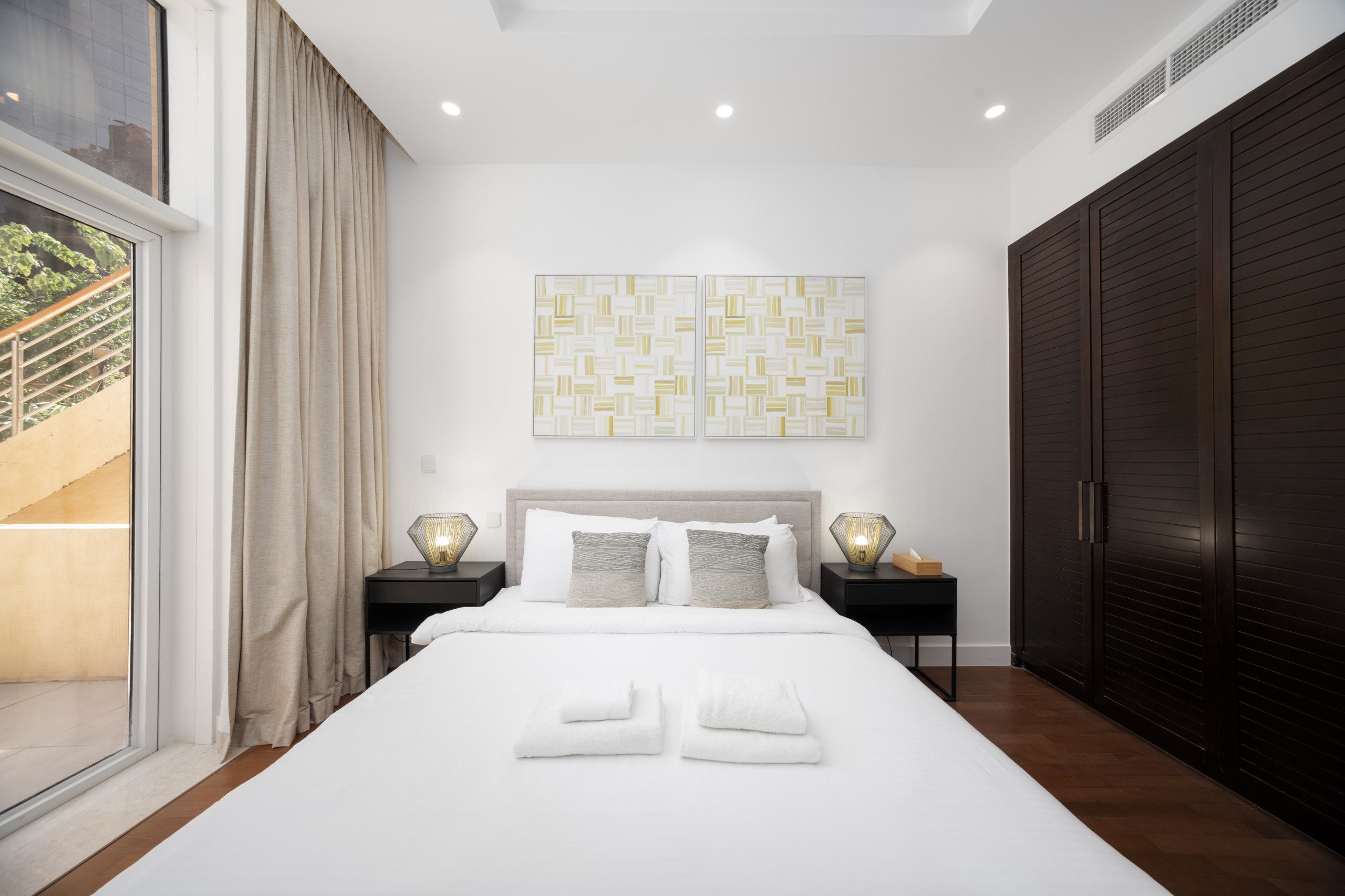 Une chambre moderne avec un grand lit, deux tables de chevet, une armoire et une fenêtre avec des rideaux.