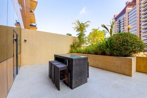 A patio area with a table and chairs, surrounded by a low wall and greenery.