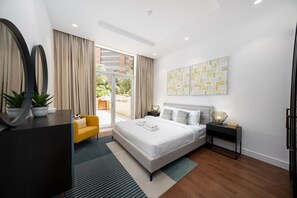 A modern hotel room with a large bed, a sofa, a desk, and a balcony with a view of the city.