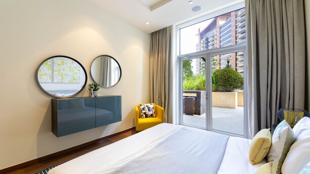 Una moderna camera d'albergo con un letto grande, una toeletta integrata, due specchi a parete e vista sull'esterno tramite una porta scorrevole in vetro.