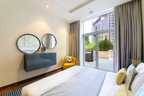 A modern hotel room with a large bed, a built-in vanity, two wall mirrors, and a view of the outside through a sliding glass door.