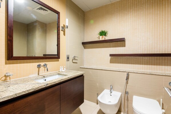 A bathroom with a sink, bidet, and toilet, wooden cabinets, and a mirror.