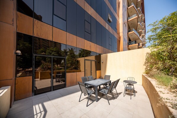 An outdoor patio with a table and chairs, a glass door entrance, and a building with a modern design.