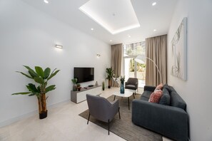 A modern living room with a flat-screen TV, grey sofa, coffee table, and potted plants.