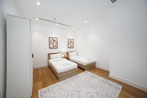A modern bedroom with two beds, a wooden floor, and a patterned rug.