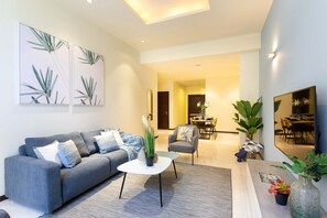 A modern living room with a grey sofa, a white coffee table, and a dining area in the background.