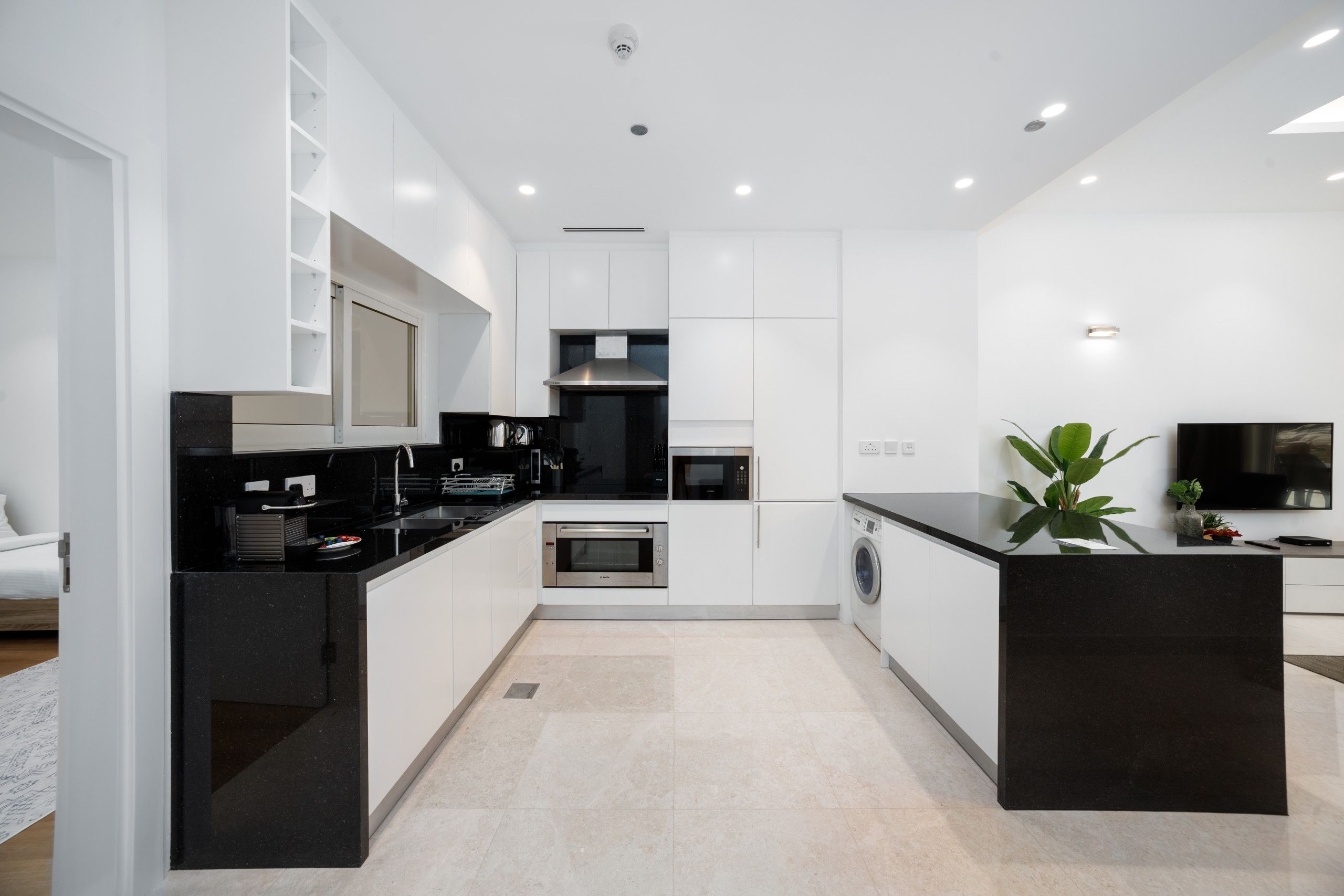 Cozinha moderna com armários brancos, bancadas pretas, forno embutido, micro-ondas e máquina de lavar.