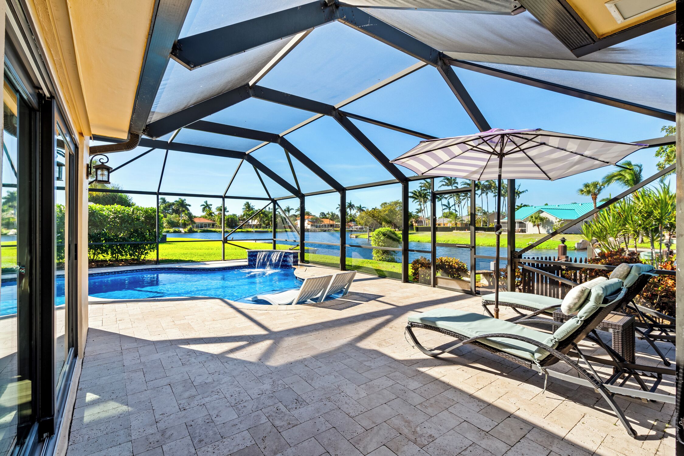 A covered outdoor area with a pool, lounge chairs, and a view of a golf course.