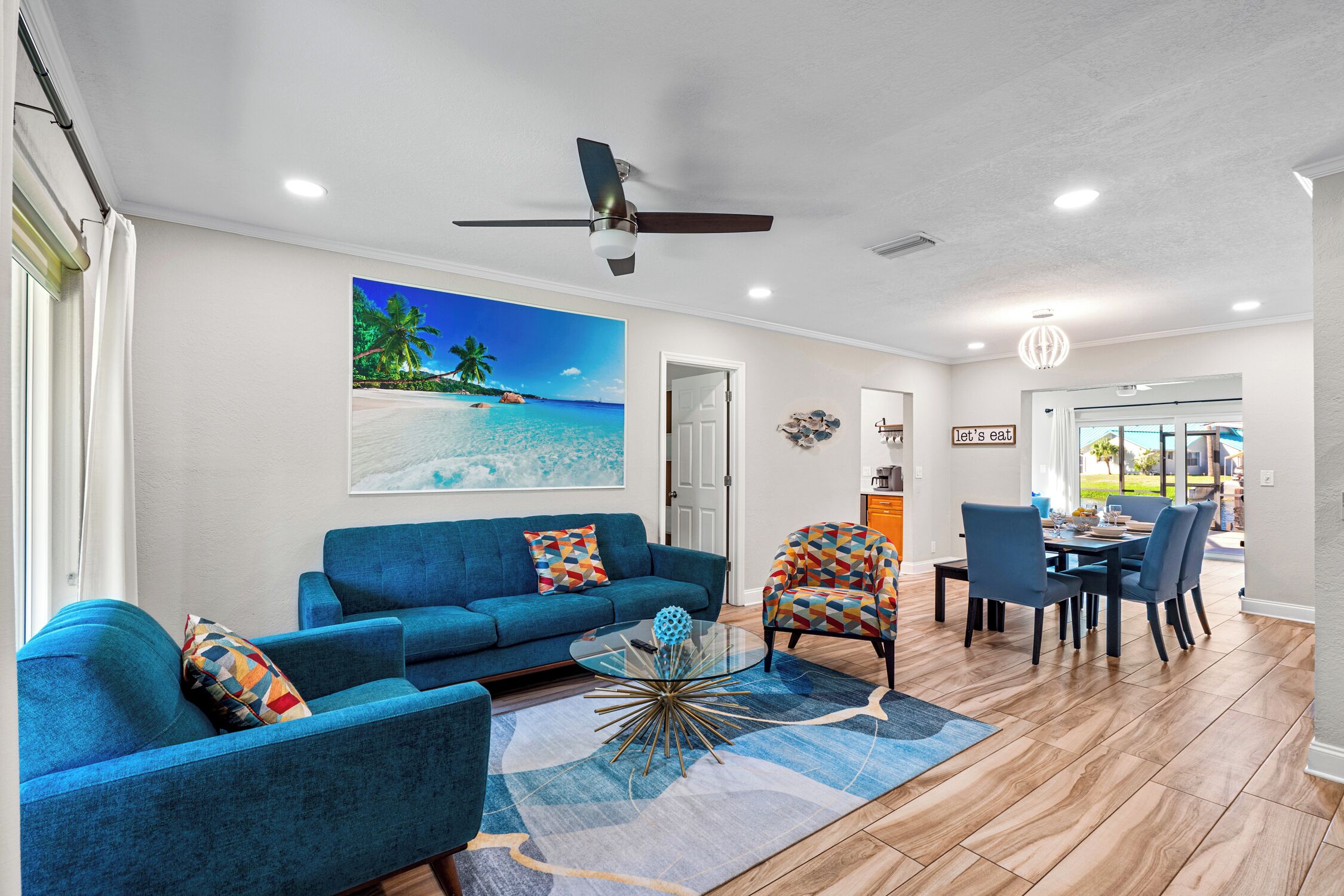Uma sala de estar com um sofá azul, uma mesa de centro de vidro e um espaço de jantar com mesa e cadeiras.