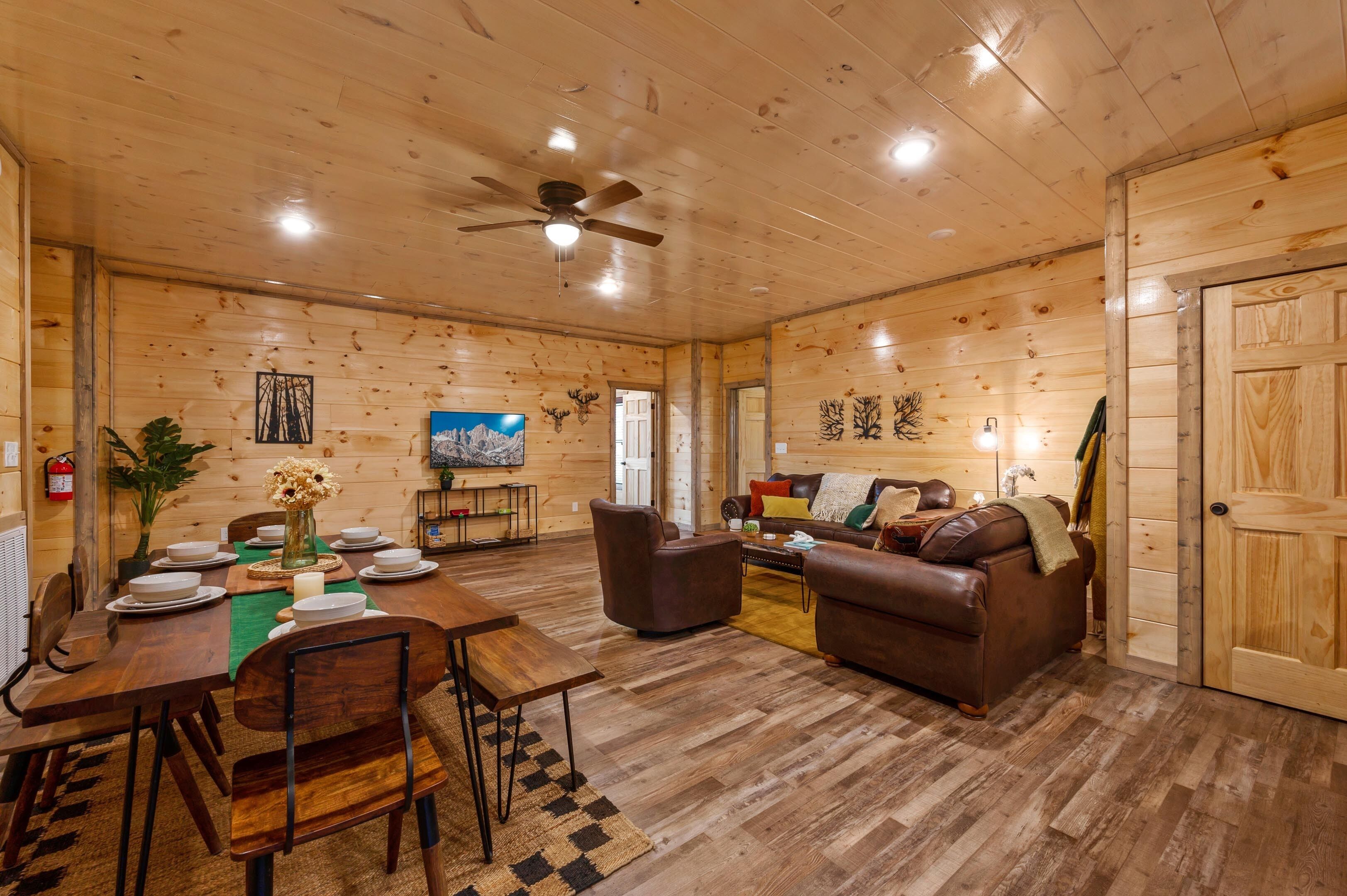 A wooden interior with a dining table set for four, two sofas, a ceiling fan, and a door.