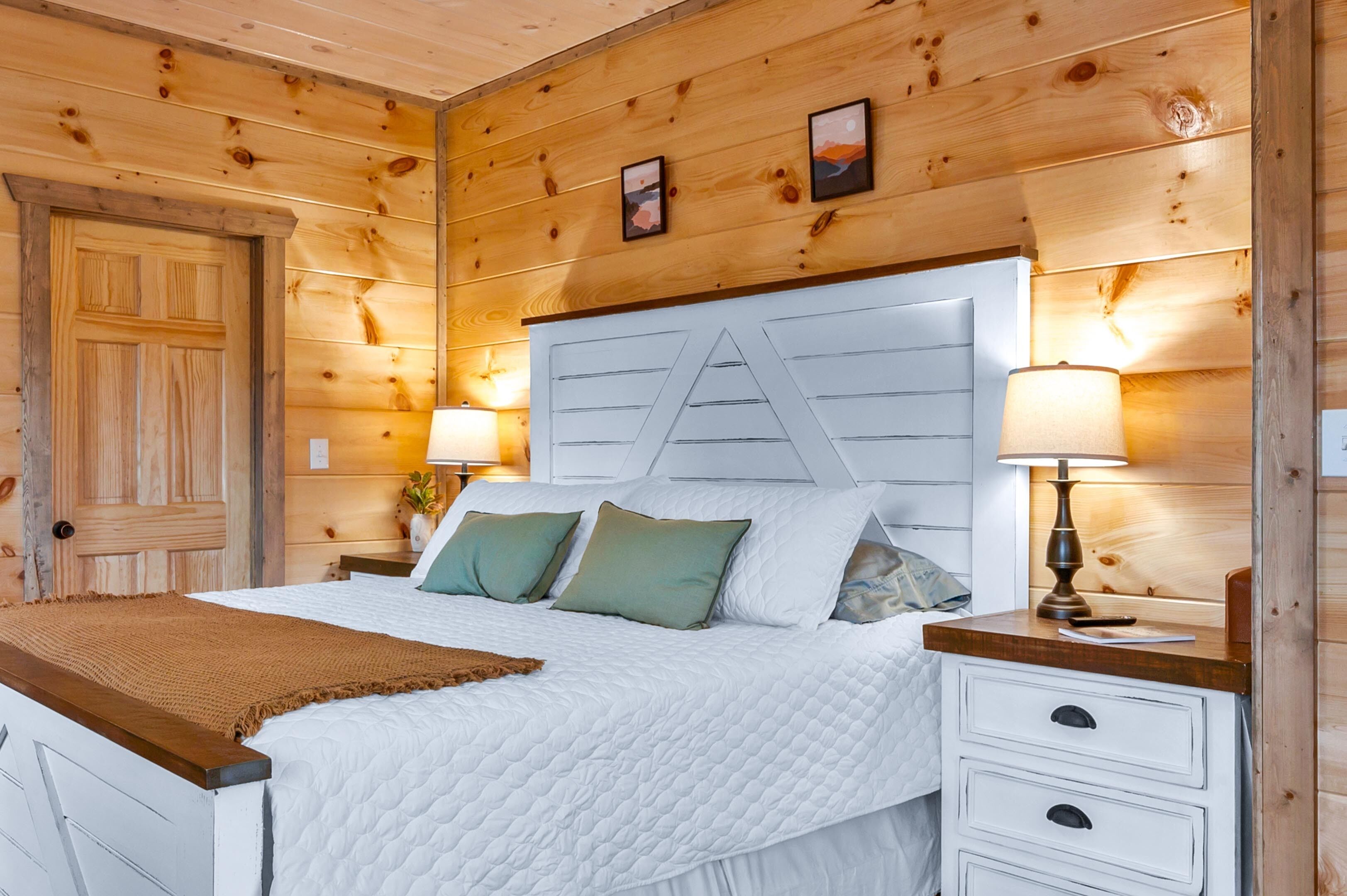 Une chambre à coucher de style cabane en bois, avec un lit, deux tables de chevet et une petite table de nuit.