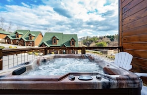 Uma banheira de hidromassagem com grades de madeira e vista para uma fileira de cabanas ao fundo.