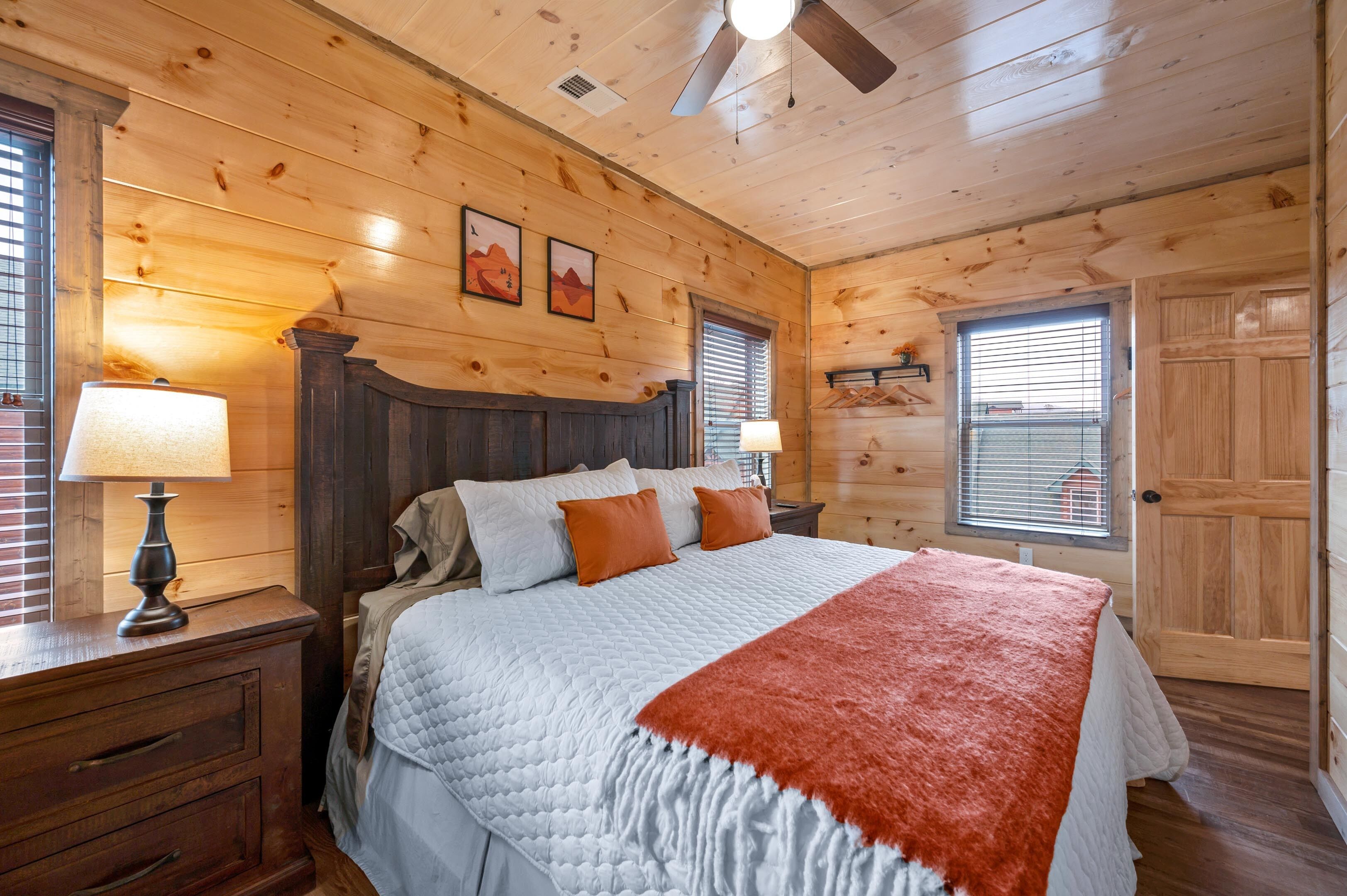 Une chambre dans une cabane en bois, avec un grand lit, deux lampes de chevet et un ventilateur de plafond.