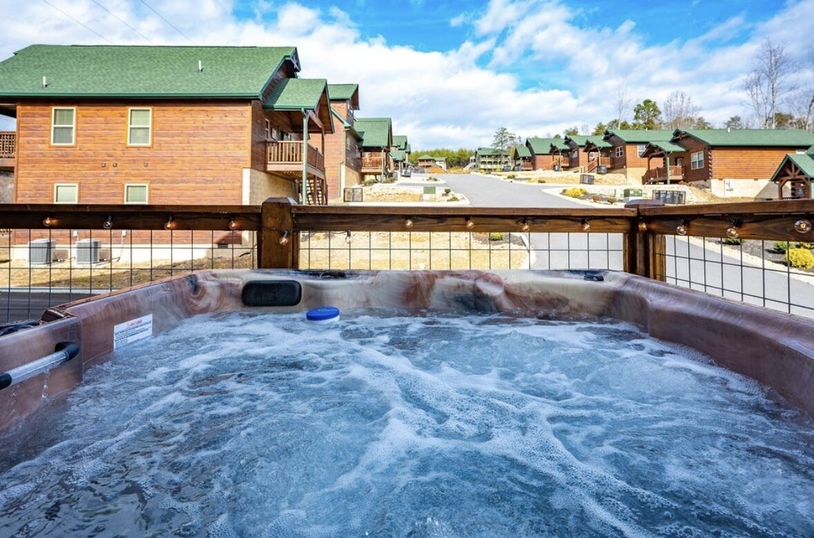 Un jacuzzi con terraza de madera y vista a una hilera de cabañas de madera con techos verdes.