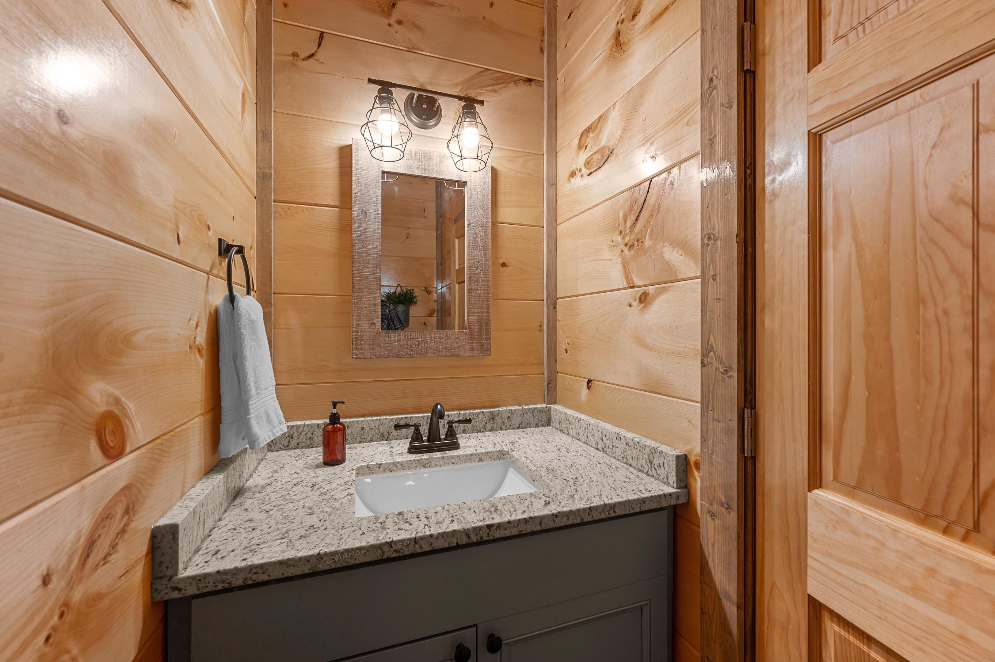 A bathroom with wooden walls, a granite countertop, a sink, a mirror, and a towel hanging on the wall.