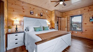 Un dormitorio con paneles de madera, una cama, mesitas de noche, un ventilador de techo y una ventana.
