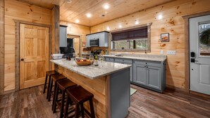 Interior de una cabaña de madera con cocina, que incluye una isla central, taburetes de bar y un microondas.