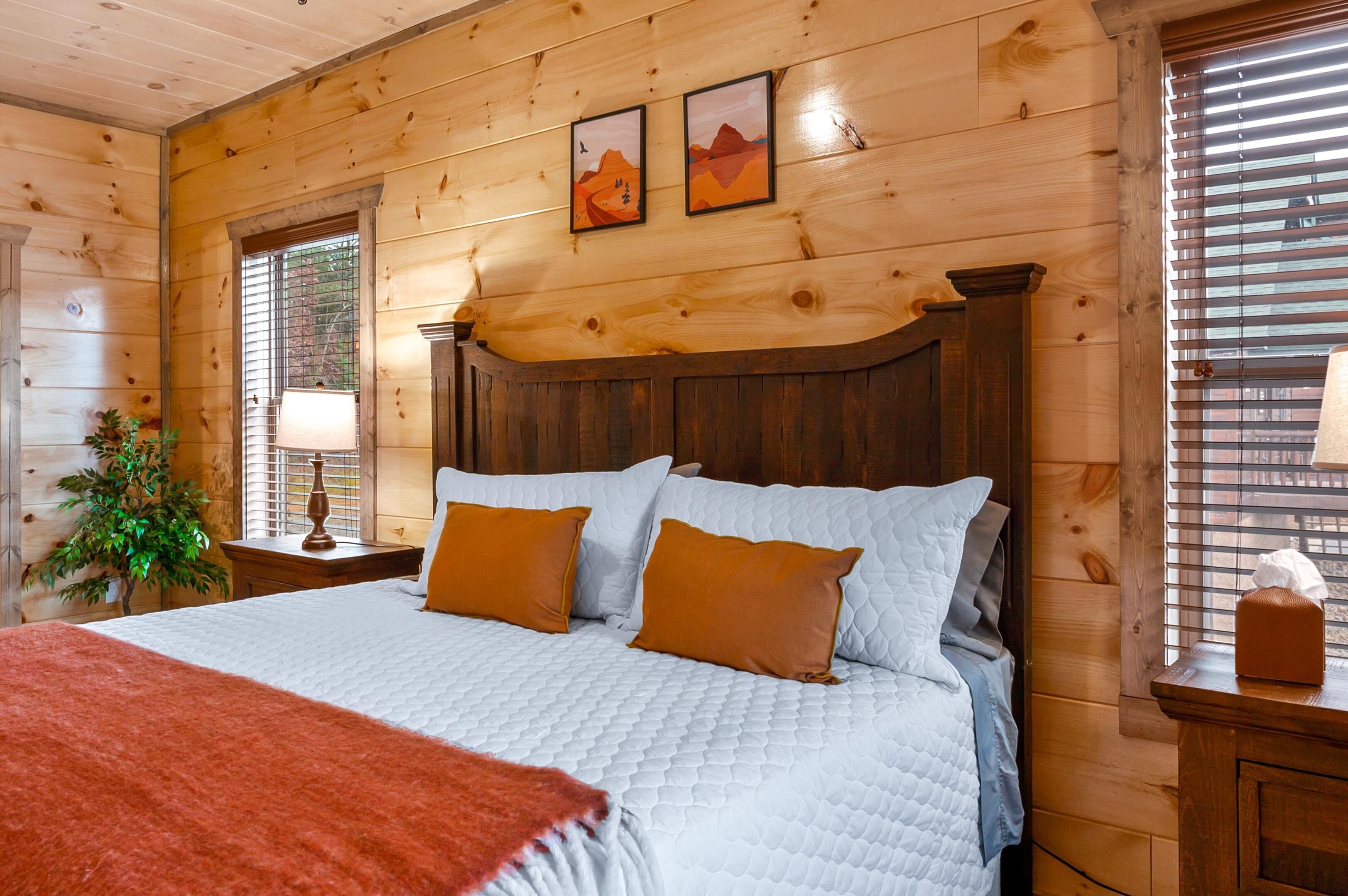 Camera da letto con pannelli in legno, un grande letto, due cuscini, un comodino, una lampada e una finestra con persiane.