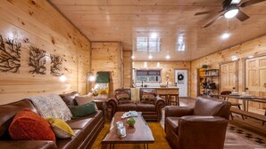 Un interior acogedor de cabaña con detalles de madera, mobiliario de cuero, una zona de comedor y una cocina.