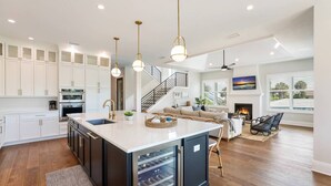 A modern kitchen with white cabinets, a large island, and a dining area with a sofa and chairs. - Bikini Bottom: 5 Hole Mini Golft, Games,3 Blocks to Beach, Dog Friendly, Pool, by Anna Maria Life (Anna Maria)