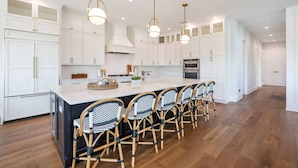 A modern kitchen with white cabinetry, a central island with bar stools, and pendant lighting. - Bikini Bottom: 5 Hole Mini Golft, Games,3 Blocks to Beach, Dog Friendly, Pool, by Anna Maria Life (Anna Maria)