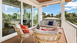 A covered outdoor area with wicker furniture and cushions, large glass doors, and a view of palm trees and buildings. - Bikini Bottom: 5 Hole Mini Golft, Games,3 Blocks to Beach, Dog Friendly, Pool, by Anna Maria Life (Anna Maria)