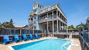 A pool area with a wooden deck, blue chairs, and a two-story building with balconies. - Oceanside, Private Pool, Pickleball Court, Ocean Views (Salvo)