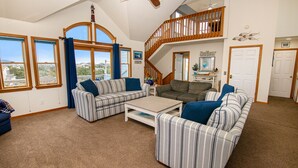 A spacious living room with a high ceiling, a staircase leading to an upper level, and large windows offering a view of the outside. - Oceanside, Private Pool, Pickleball Court, Ocean Views (Salvo)