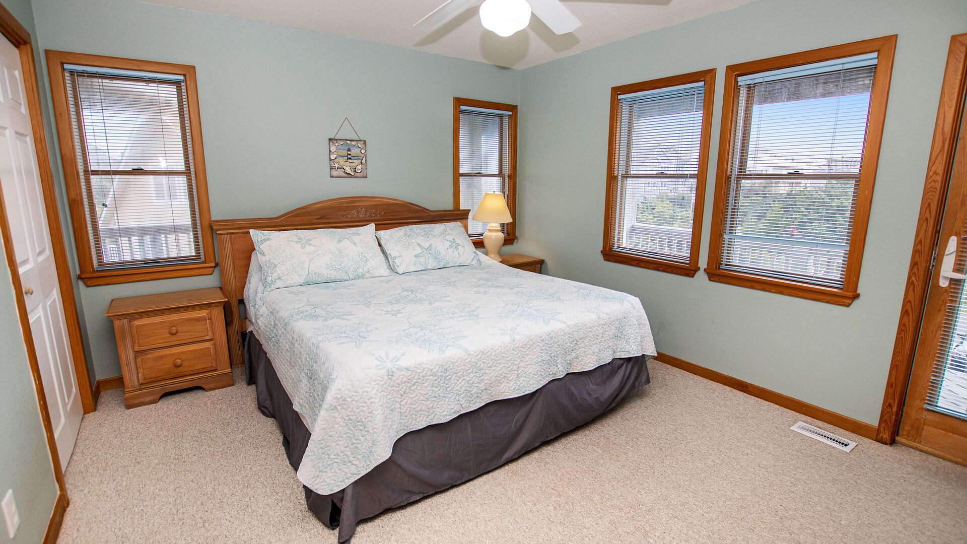 A bedroom with a bed, two nightstands, a lamp, and three windows with blinds.