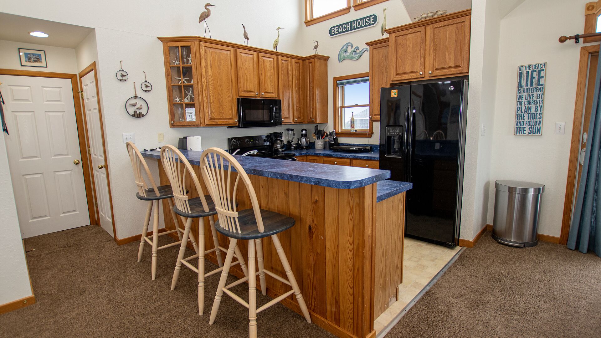A kitchen with wooden cabinets, a black refrigerator, a blue countertop, and three wooden bar stools.