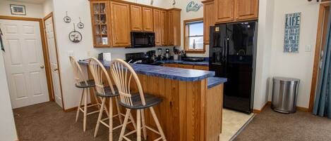 A kitchen with wooden cabinets, a black refrigerator, a blue countertop, and three wooden bar stools.