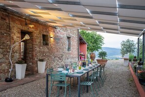 Ein überdachter Essbereich im Freien mit einer Steinwand, einem gedeckten Tisch und Blick auf die Landschaft.