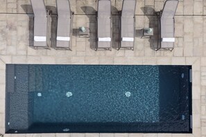 Eine Vogelperspektive auf einen Swimmingpool mit sechs Liegestühlen und einem Tisch, umrahmt von Steinfliesen.