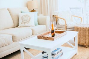 Ein Wohnzimmer mit einem weißen Sofa, einem Holztisch mit Flasche und Gläsern sowie einem Bücherregal mit Büchern.